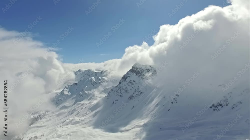 Snowy mountain shrouded in clouds on sunny day. Aerial backward low speed and blue sky for copy space Snowy mountain shrouded in clouds on sunny day. Aerial backward low speed and blue sky for copy space