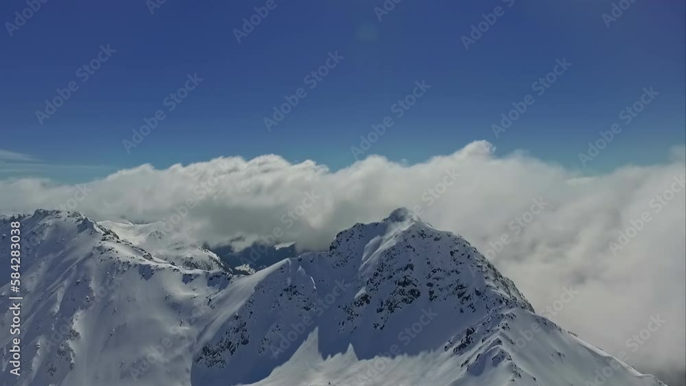 Snowy mountain shrouded in clouds on sunny day. Aerial forward low speed and blue sky for copy space Snowy mountain shrouded in clouds on sunny day. Aerial forward low speed and blue sky for copy space