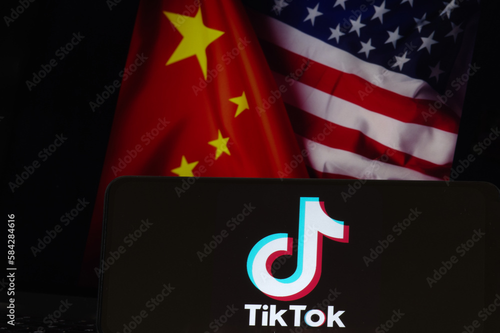 TikTok logo seen on the silhouette of smartphone with American and Chinese flags on the back. US