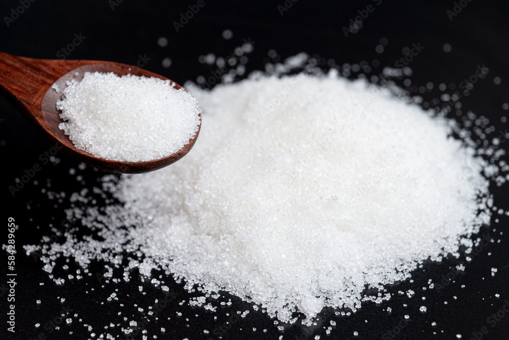 Close-up white sugar in a wooden spoon. Dark and Moody background. Close-up white sugar in a wooden spoon. Dark and Moody background.