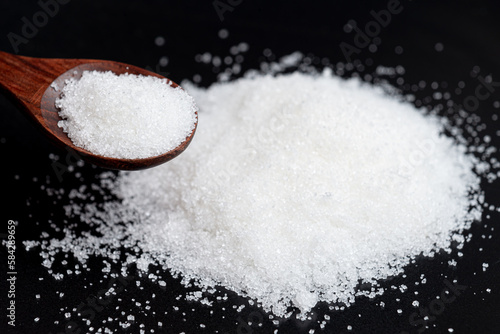 Close-up white sugar in a wooden spoon. Dark and Moody background.