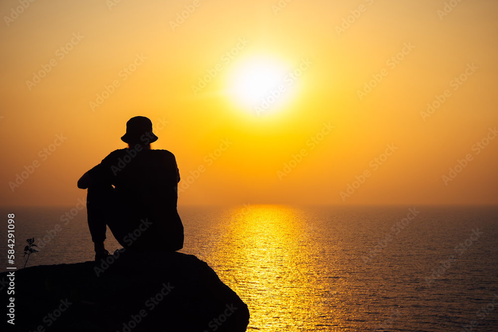 The silhouette of a man in a cap against the background of a bright sunset and the endless sea. A thoughtful adventurer, thoughts about the future and the meaning of life