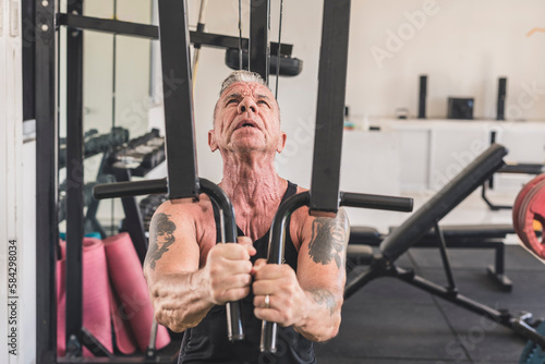A rugged and tattooed older german man does a set of chest flyes on the pec deck machone. Working out pectoral muscles.