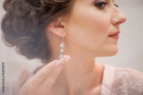 Wedding day. Bride morning. Makeup for the bride. Wedding make-up. Bride portrait. Beautiful young girl. Portrait. Married Wedding. Professional makeup. Bride in a diadem. Girl puts on earrings
