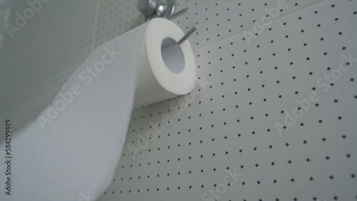 Roll of toilet paper on cardboard tube unrolled in tissue holder in restroom closeup. New soft toilet paper hangs on tile wall in bathroom photo