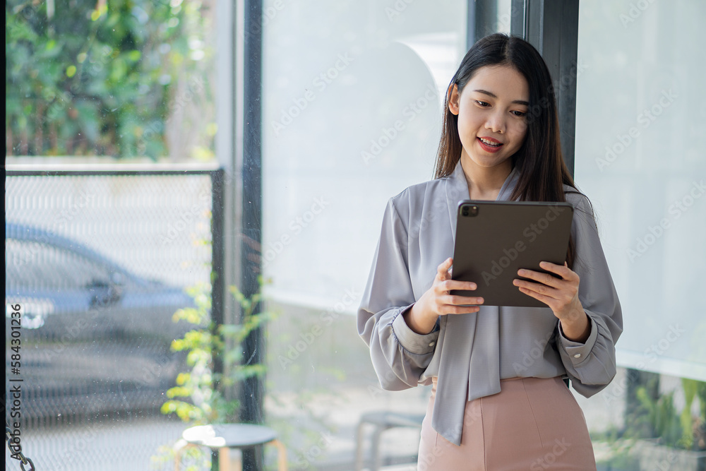 Asian woman relaxing hands using tablet surfing internet writing diary smiling cheerfully while sitting in cafe near large window Asian woman relaxing hands using tablet surfing internet writing diary smiling cheerfully while sitting in cafe near large window