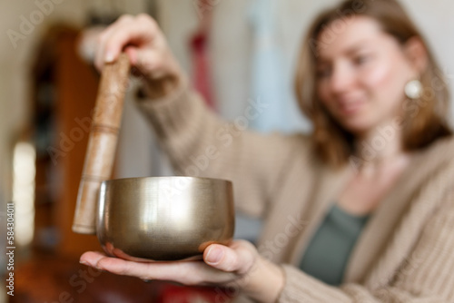 Young woman playing on a singing tibetian bowl.Relaxation and meditation.Sound therapy alternative medicine.Buddhist healing practices.Clearing space of negative energy.Selective focus close up. 