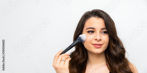 Young happy smiling woman applying contouring or blush on cheeks with big brush.