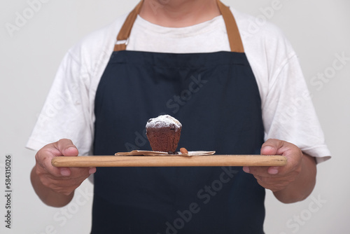 A double chocolate muffin with sliced almonds on top sprinkled with powdered sugar, served on a wooden tray by a male waiter wearing black apron. photo