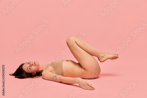 Relaxed and calm. Self-love and acceptance. Portrait of young girl in beige underwear posing against pink studio background. Concept of body and skin care  figure  fitness  health  wellness.