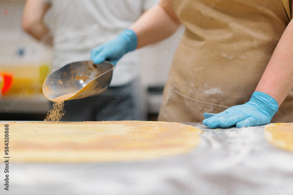 Fototapeta premium The kitchen in the bakery - the process of making cinnabons, the woman baker adds cinnamon and chocolate to the dough