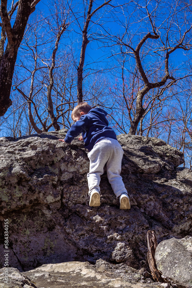 Naklejka premium Young toddler boy crawling along rock boulders while hiking up Cheaha mountain in Alabama state park and campground