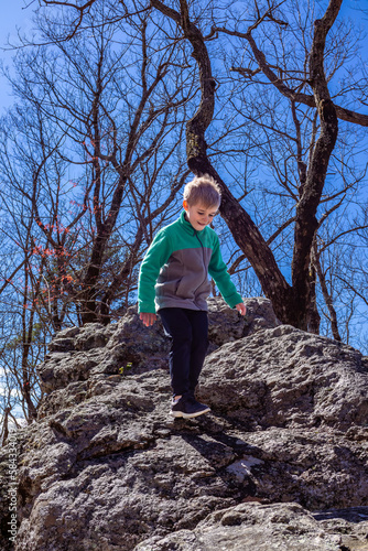 Young boy climbing along rock boulders while hiking up Cheaha mountain in Alabama state park and campground