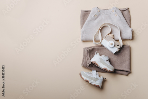 Fototapeta Naklejka Na Ścianę i Meble -  Baby stuff and accessories. Set of knitted clothes - sweater, pants, shoes, wooden camera toy. Baby shower concept. Flat lay, top view. Copy space. Fashion children's clothing, shoes