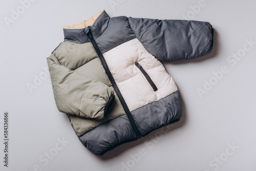 Fashion baby colorblock puffer jacket on grey background. Top view, flat lay. Newborn beige clothes outfit. Winter, autumn collection. Template with copyspace for brand, logo, advertising. Banner