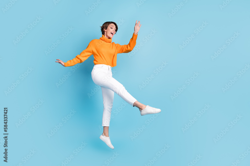 Full body photo of attractive young woman jump dance enjoy lightness elegant dressed stylish orange look isolated on blue color background