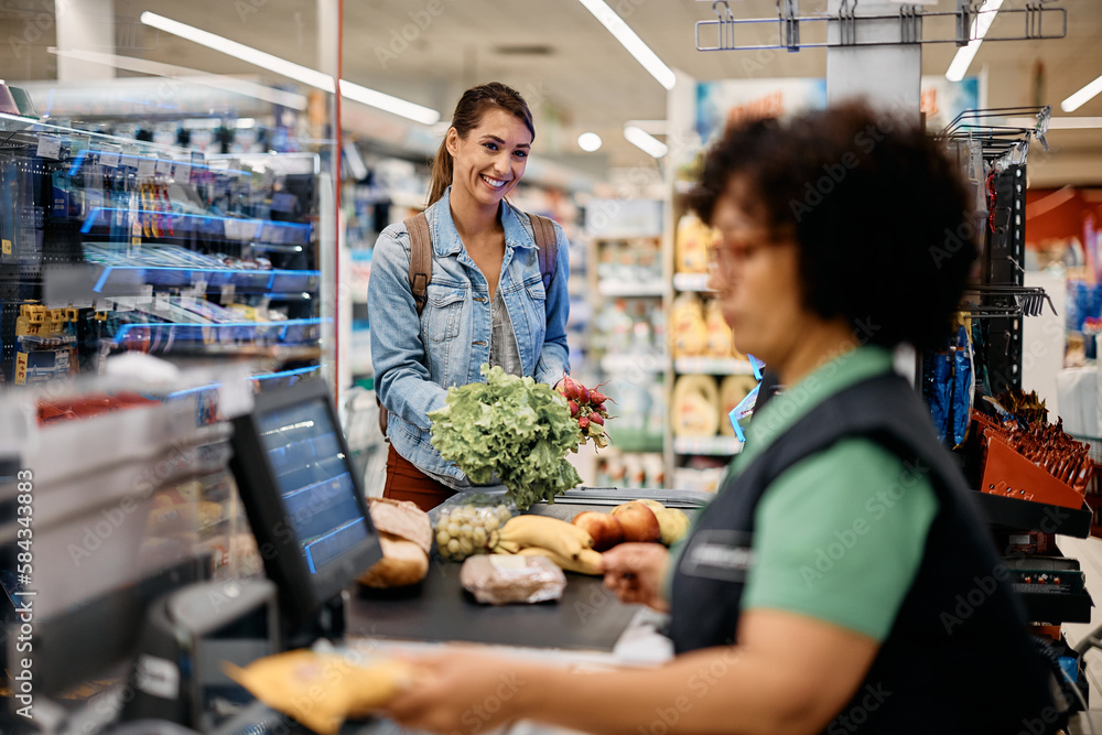 Happy woman putting groceries on checkout counter while buying in supermarket.