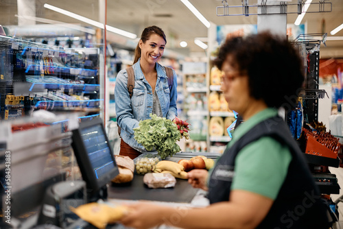 фотографія Happy woman putting groceries on checkout counter while buying in supermarket