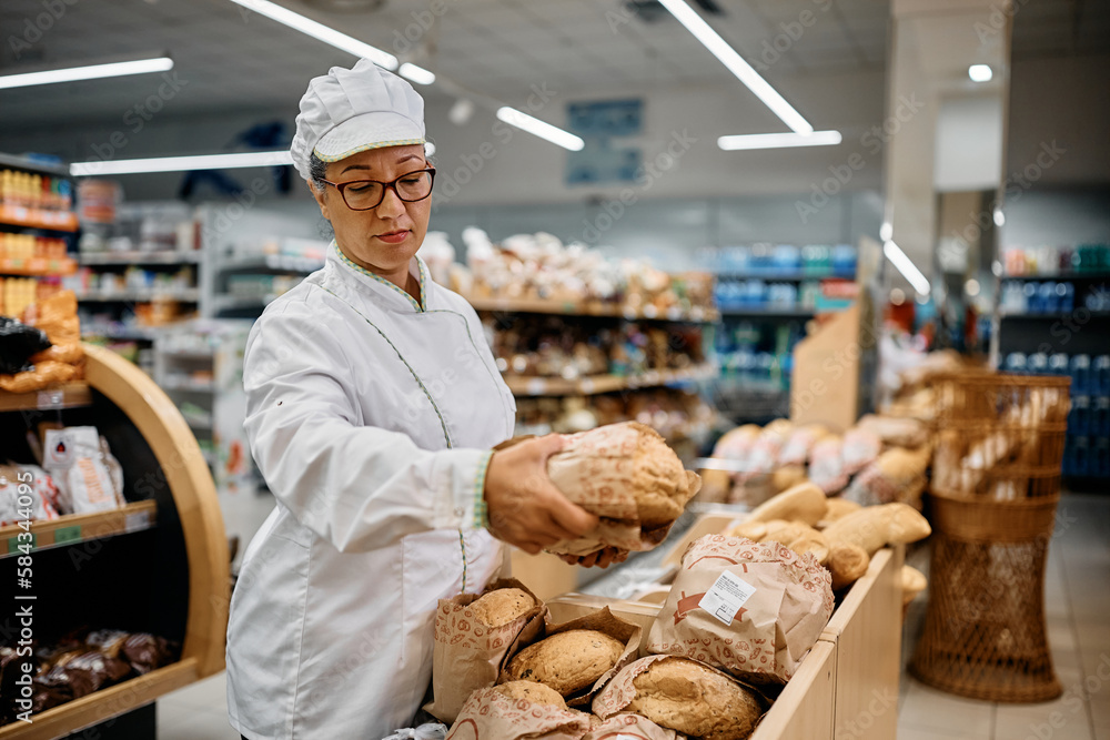 Supermarket baker arranging fresh bread on shelf.