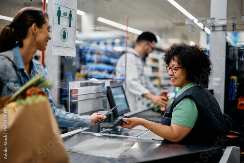 Foto Happy woman pays with her smart phone while buying at supermarket