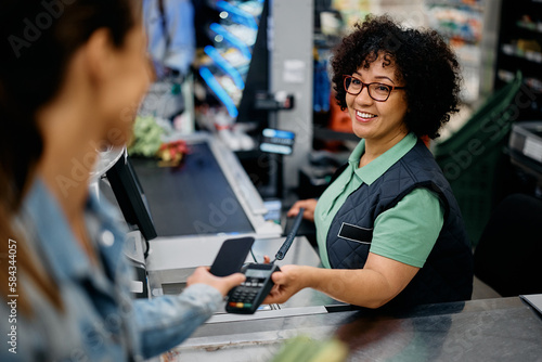 Happy cashier holds credit card reader while customer is paying with smart phone at supermarket. photo