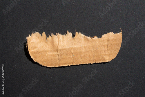 Torn cardboard piece isolated on a black background. Ripped paper.
