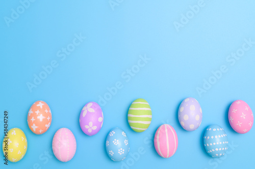 Happy Easter holiday greeting card design concept. Colorful Easter Eggs and spring flowers on blue background. Flat lay, top view, copy space.