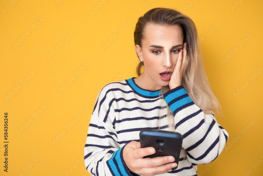 Scared young woman with mobile phone, isolated on yellow background. Shocked girl holding smartphone. Unbelievable Scared young woman with mobile phone, isolated on yellow background. Shocked girl holding smartphone. Unbelievable