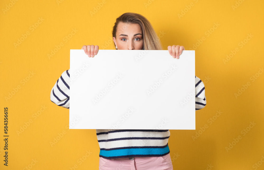 Surprised face of young women behind white board, isolated on yellow background. One girl showing blank empty paper billboard with blank space near her head Surprised face of young women behind white board, isolated on yellow background. One girl showing blank empty paper billboard with blank space near her head