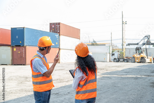 two asian industrial engineer man and woman wearing safety vest and helmet. Foreman talking with worker or laborer in the Industrial Container Cargo.