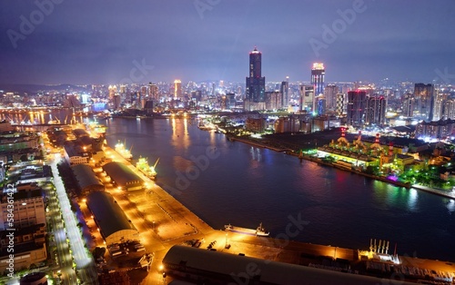 Aerial skyline of Kaohsiung at dusk, a vibrant seaport city in Southern Taiwan, with 85 Sky Tower next to Exhibition Center by the harbor and Shoushan Mountain under blue night sky in background