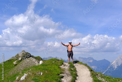 tanned mature man with naked torso smiles victoriously on top of mountain, on crest of pass, active lifestyle, mountaineering, concept trekking and hiking in mountains, extreme sports, victory