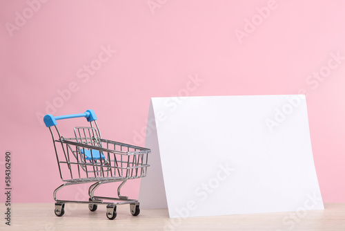 Mini shopping trolley with blank white paper calendar or table flyer mockup on pink background