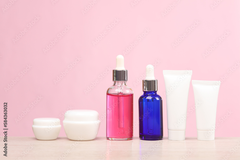 Face serum bottles, cream tubes and jars on the table, pink background. Skin health and youth concept Face serum bottles, cream tubes and jars on the table, pink background. Skin health and youth concept