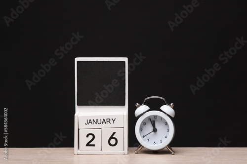 White wooden block monthly calendar with the date january 26 and alarm clock on the table, black blackbackground. Planning