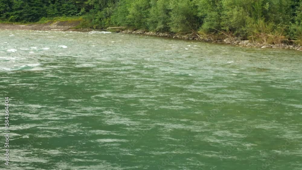Close up of a wild mountain river with a strong current. Shades of deep green water, rocks in the river bed visible, creating a beautiful natural scenery. Slow motion Close up of a wild mountain river with a strong current. Shades of deep green water, rocks in the river bed visible, creating a beautiful natural scenery. Slow motion