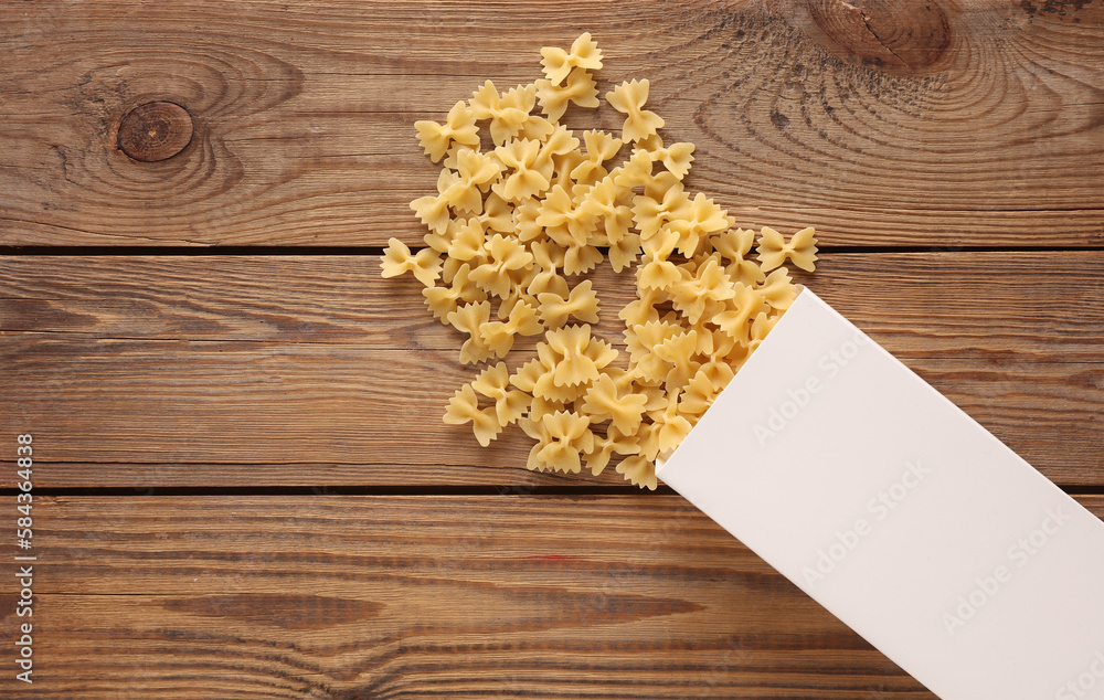 Mockup of a white box with scattered pasta bows on wooden table. Top view. Template for design Mockup of a white box with scattered pasta bows on wooden table. Top view. Template for design