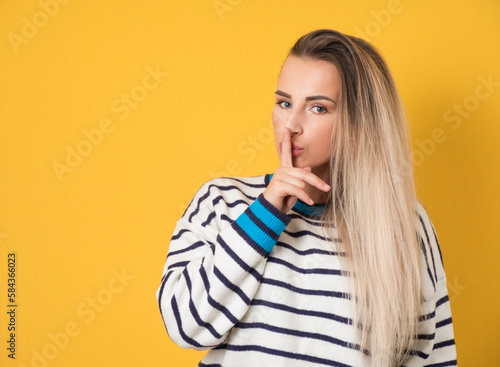 Hush. Woman holding finger on lips, keep the secret concept, isolated on yellow background