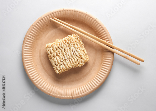 Dry briquette of instant noodles on a plate with chinese chopsticks on a gray background