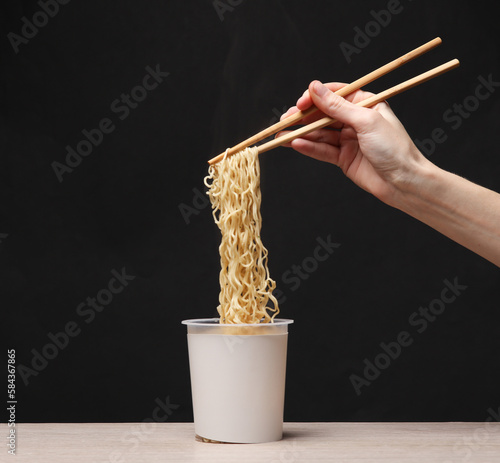 Woman\'s hand holding chinese chopsticks with instant noodles on black background. Creative mockup