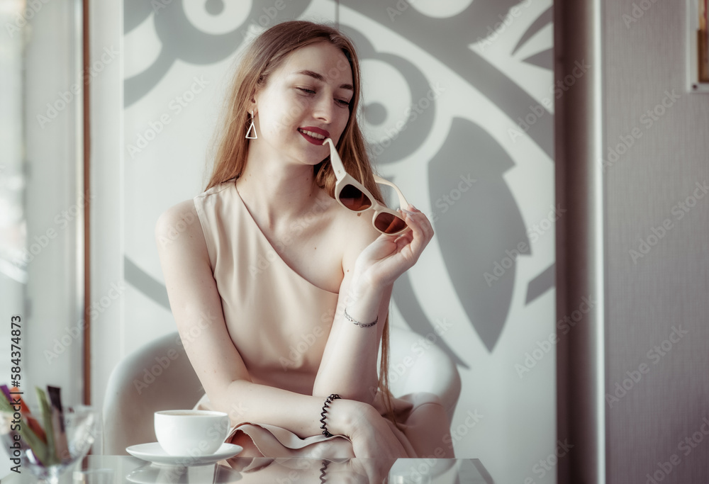 Stylish smiling young woman sitting alone at a table in a cafe