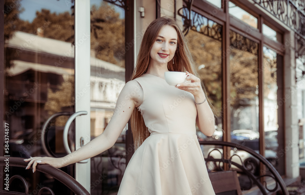 Beautiful woman in a dress stands on the porch of cafe with coffee cup Beautiful woman in a dress stands on the porch of cafe with coffee cup