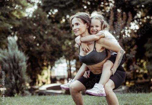 Athletic mom squatting with her little daughter outdoors, healthy lifestyle, fitness active family concept. Training together