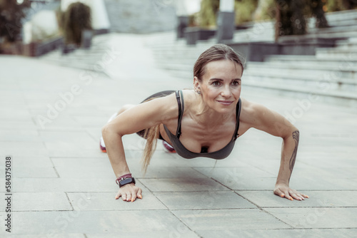 Young smiling fit woman practicing push-ups outdoors. Healthy lifestyle concept