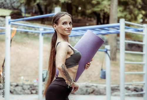 Athletic woman with perfect body posing with yoga mat on sports ground