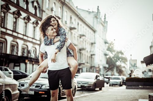 Couple in love. Man carrying girl on his back in the street. Smiling man with beautiful young woman  ride piggyback  having fun together. Relationship concept.