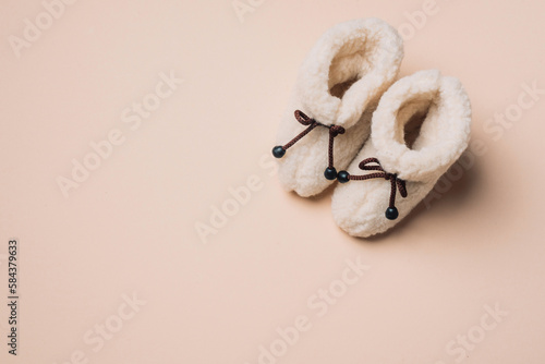 Woolen booties for a newborn baby, soft sheep toy on beige background. Top view, flat lay. Copy space