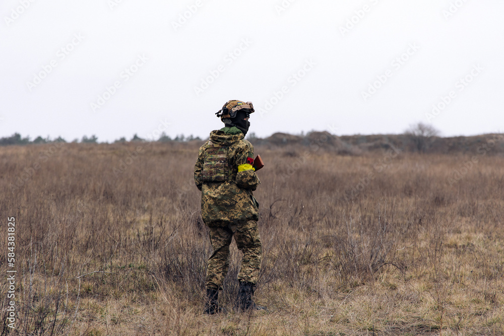 Rear view of armed Ukrainian soldier walking in steppe in uniform and helmet. Rear view of armed Ukrainian soldier walking in steppe in uniform and helmet.