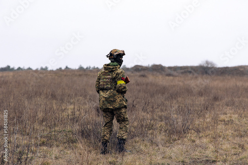 Rear view of armed Ukrainian soldier walking in steppe in uniform and helmet.
