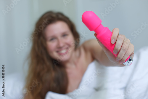 Foto Young happy sexy woman hold in hand sex toy, masturbate with vibrator in bed in bedroom at home
